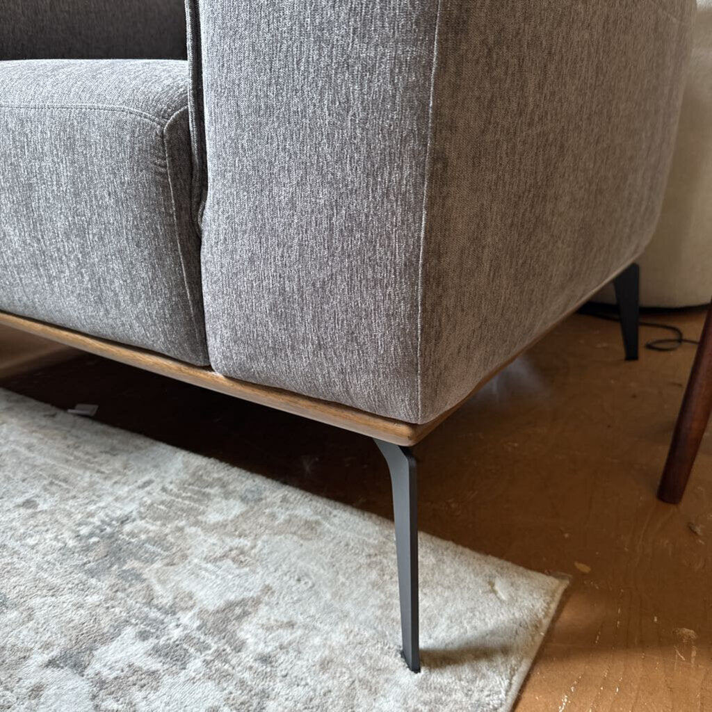 Gray upholstered chair with wooden base on a carpeted floor