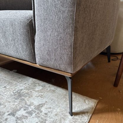 Gray upholstered chair with wooden base on a carpeted floor
