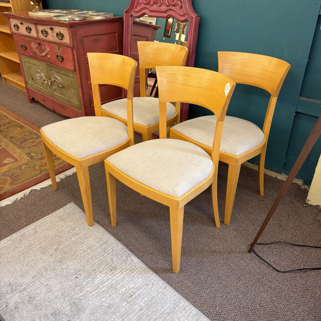 Four wooden chairs with beige cushions in a room with a dresser and mirror.