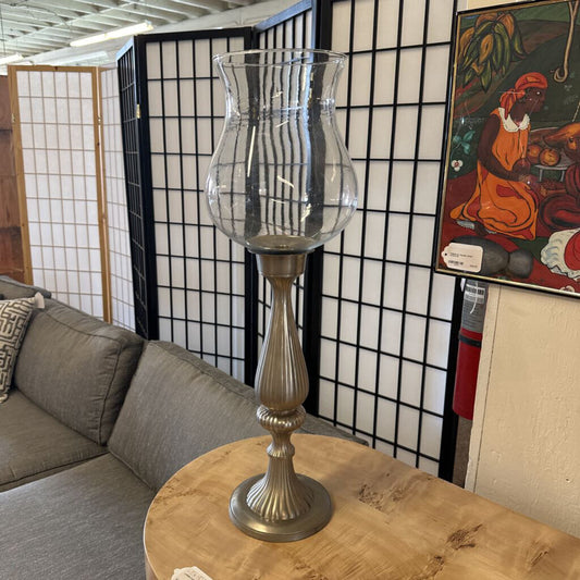 Decorative silver candle holder on a wooden table with a couch and artwork in the background