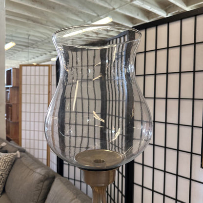Clear glass lantern on a stand against a tiled wall