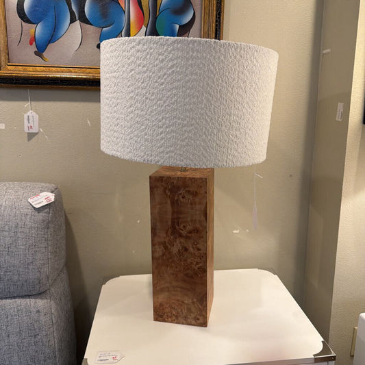 Table lamp with wooden base and textured white shade on a table in a room setting.