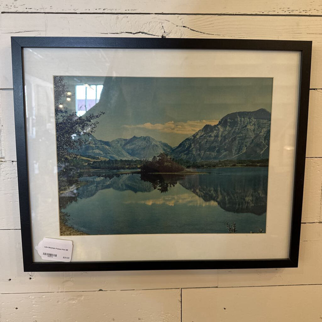 Framed landscape print of a mountain lake on a wooden surface