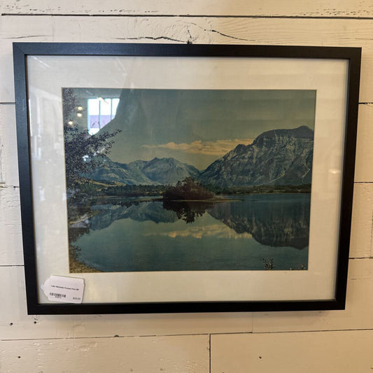 Framed landscape print of a mountain lake on a wooden surface
