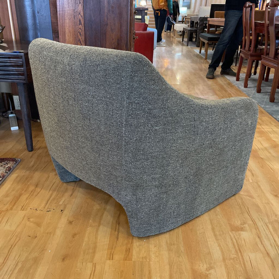 Gray upholstered chair on a wooden floor with a blurred background of a store interior.