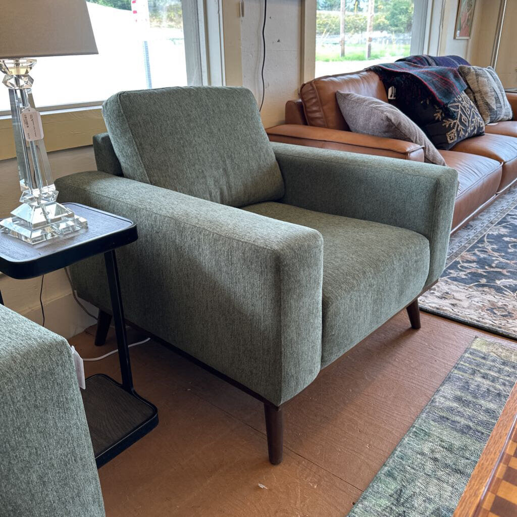 Green armchair in a living room setting with a brown sofa and lamp.