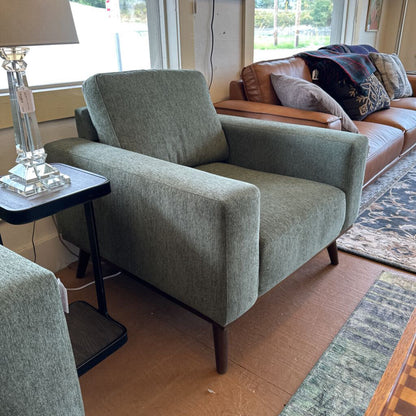 Green armchair in a living room setting with a brown sofa and lamp.