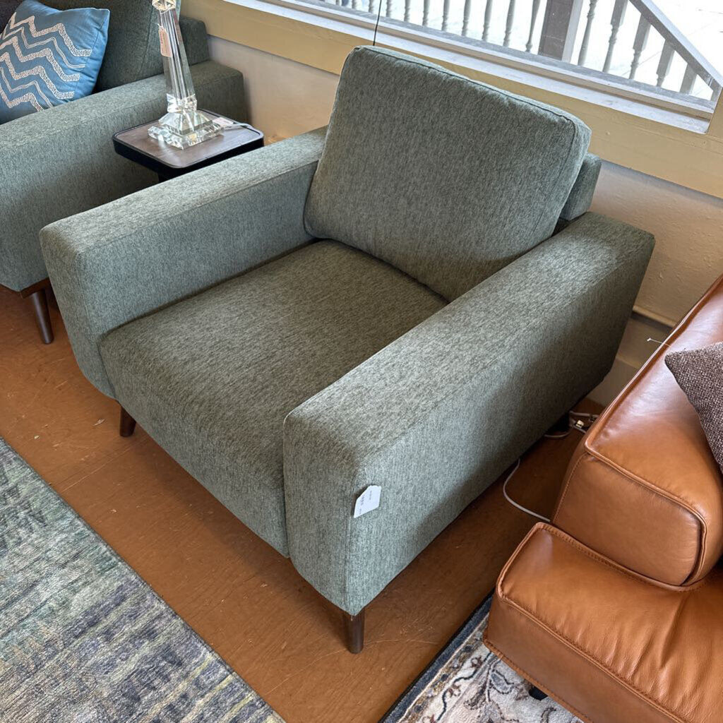 Gray upholstered armchair in a living room setting with a brown leather chair and blue cushioned chair.