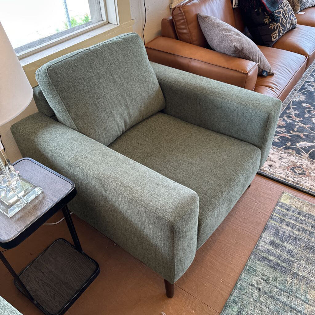 Green armchair in a living room with a brown sofa and lamp.