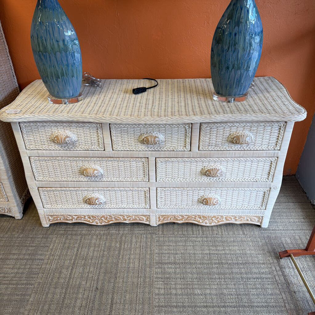 White wicker dresser with six drawers and two blue vases on top against an orange wall.
