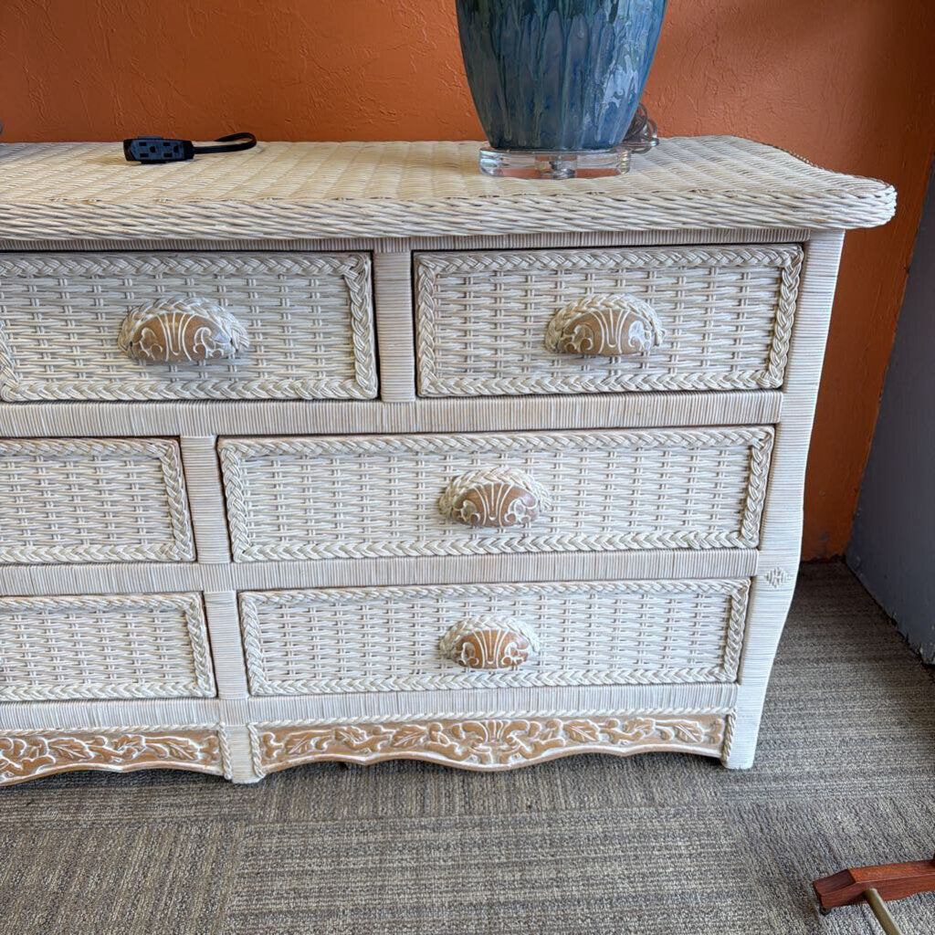 Wicker dresser with shell-shaped handles against an orange wall.