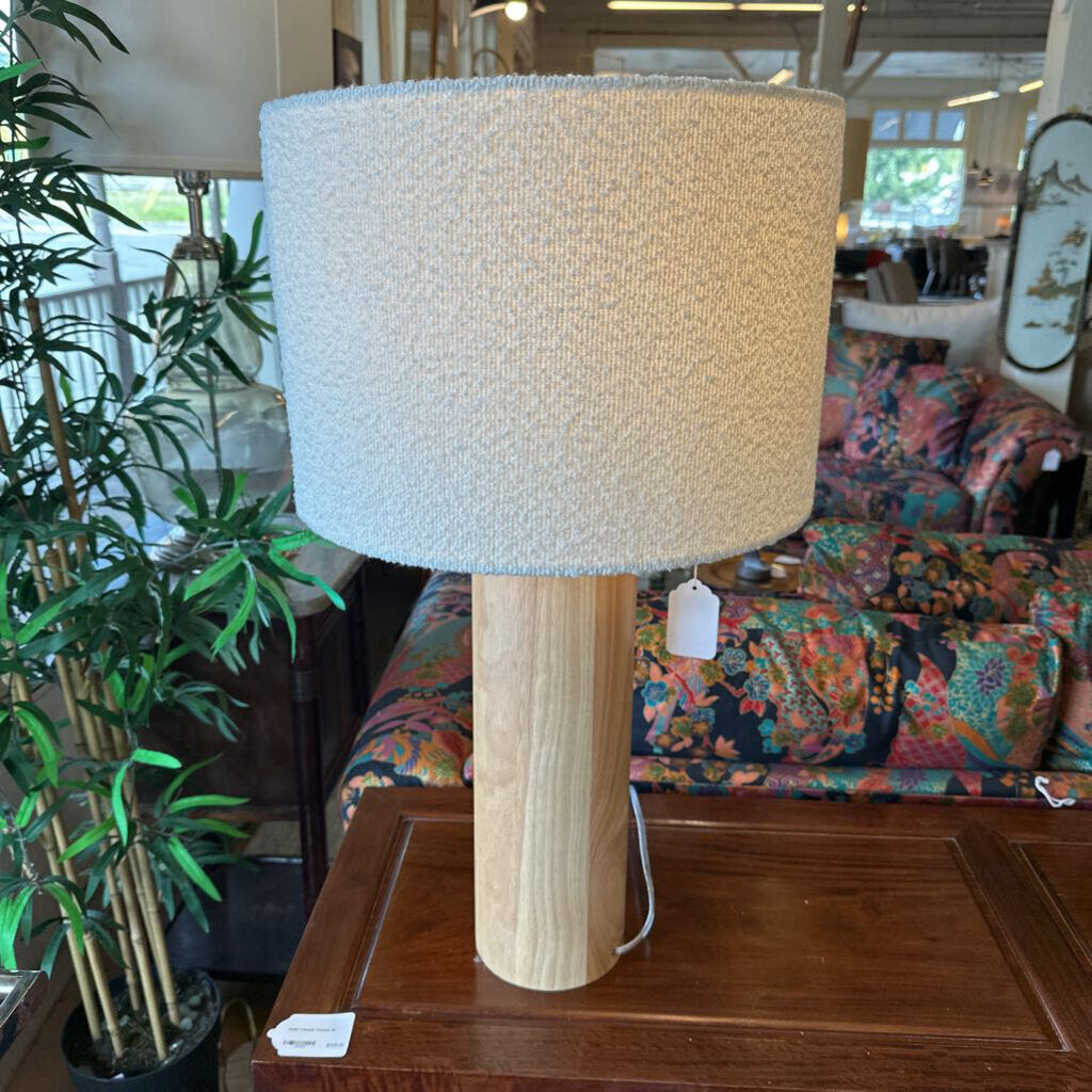 Table lamp with a textured beige shade on a wooden base in a store setting.