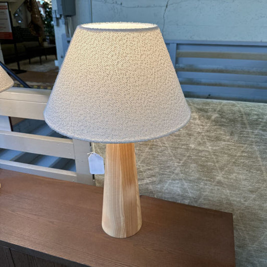 Table lamp with wooden base and textured beige shade on a wooden surface.