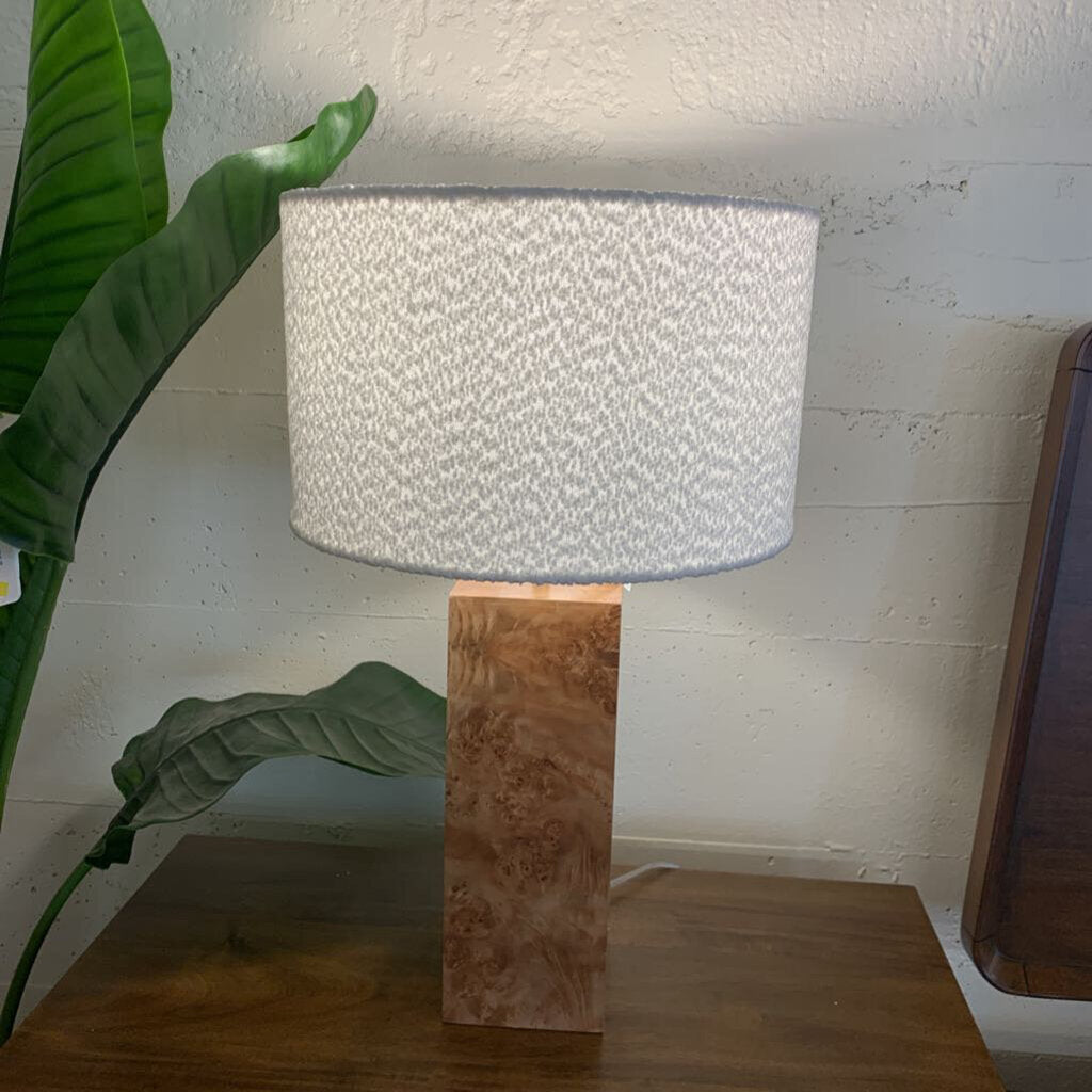 Table lamp with textured white shade on a wooden base next to a plant