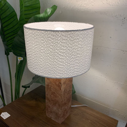 Lamp with a textured white shade on a wooden base next to a plant.
