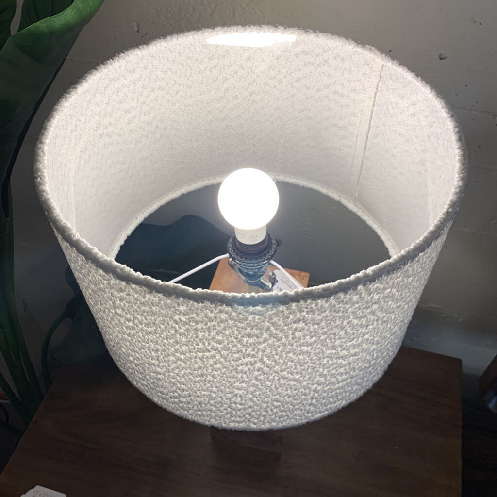 White textured lampshade with a light bulb inside on a wooden surface.