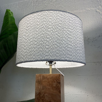 Lamp with a textured gray shade on a wooden base against a light gray wall.