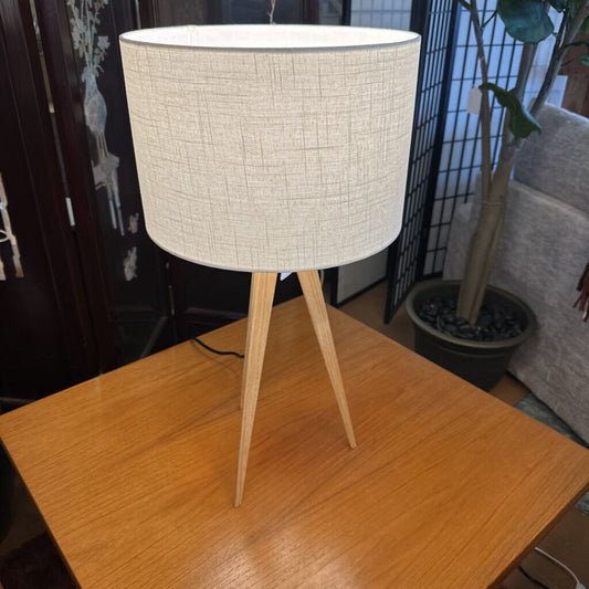 Table lamp with a white textured shade and wooden legs on a wooden table.