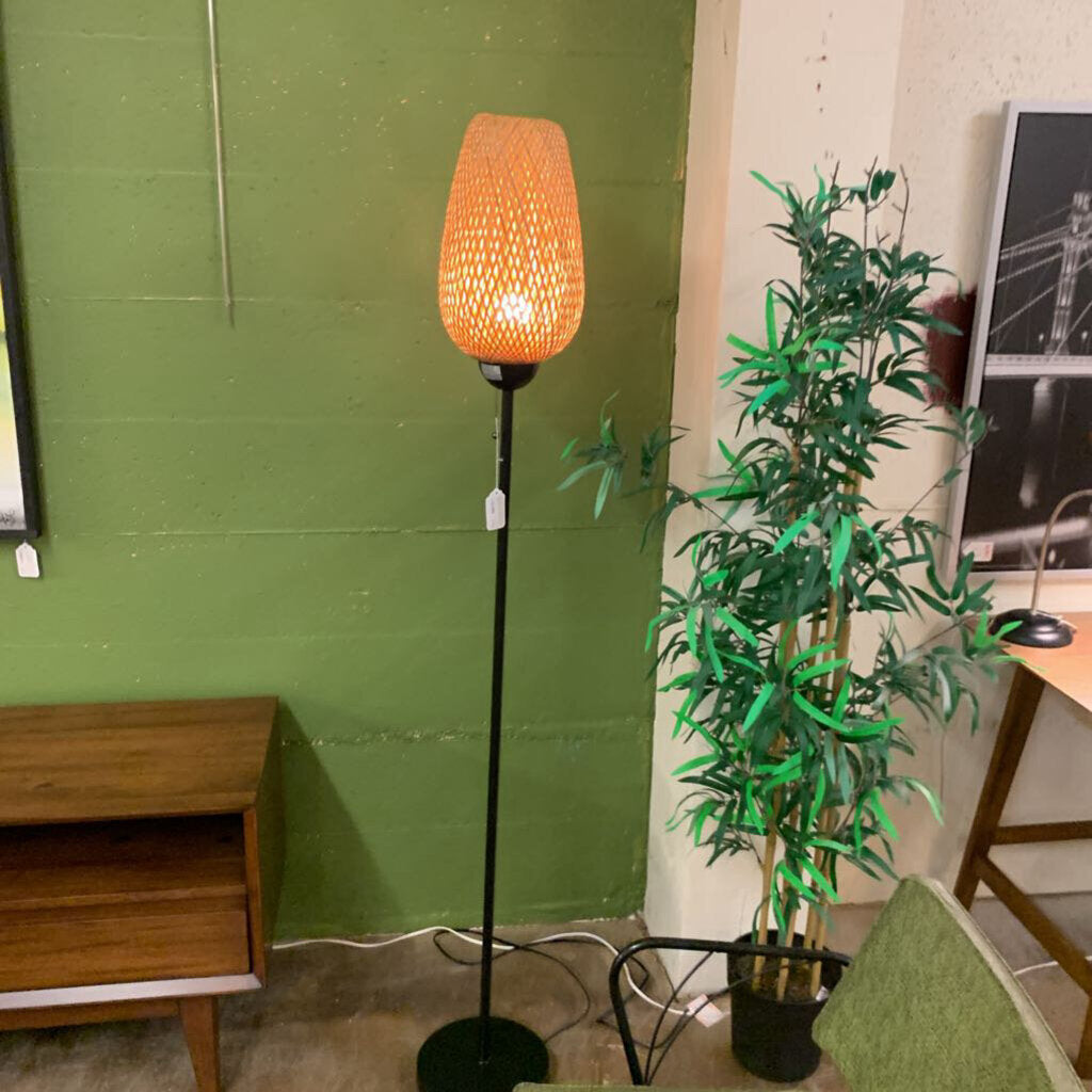 Floor lamp with orange shade in a room with green wall and wooden furniture.