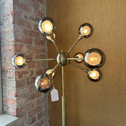 Modern floor lamp with multiple lights against a brick wall and wooden panel.
