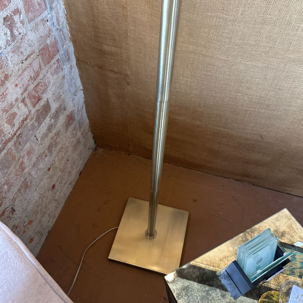 Metal floor lamp with a square base against a textured wall.