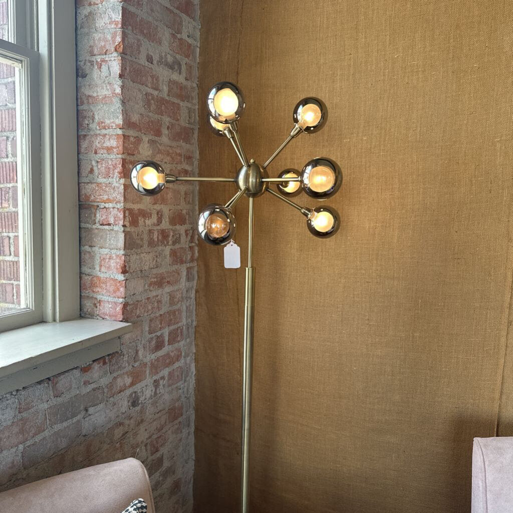 Modern floor lamp with multiple lights in a room with brick wall and window.