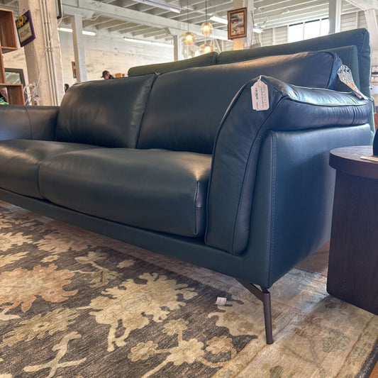 Blue leather sofa in a store setting with a patterned rug underneath.
