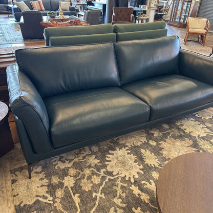 Green leather sofa in a room with patterned rug and chairs.