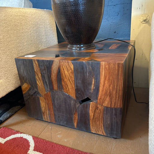 Wooden side table with a textured black lamp on top in a room setting.