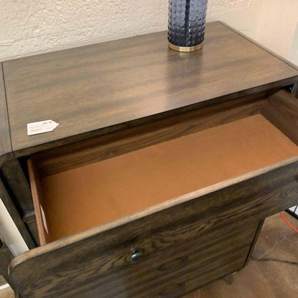 Wooden dresser with an open drawer, showing a brown interior, on a textured wall background.