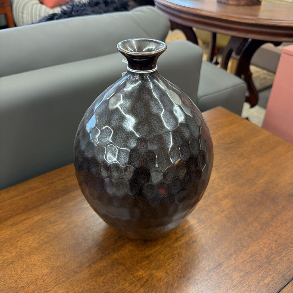 Black textured vase on a wooden table with a blurred indoor background