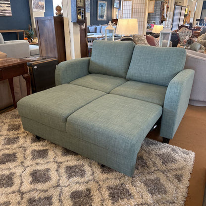 Green sofa in a showroom setting with other furniture and decor items.