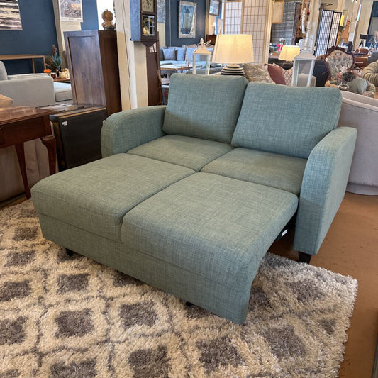 Green sofa in a showroom setting with other furniture and decor items.