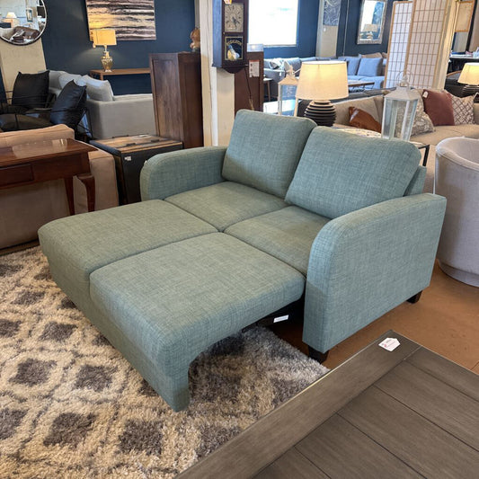 Green sectional sofa in a showroom setting with other furniture.
