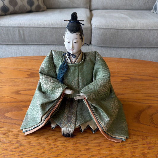 Traditional Japanese doll in green kimono on a wooden table with a gray sofa in the background