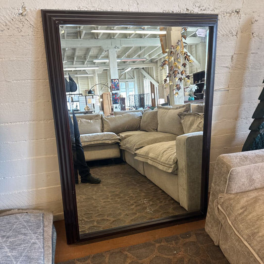 Large floor mirror reflecting a living room with beige sofa and decorative items.