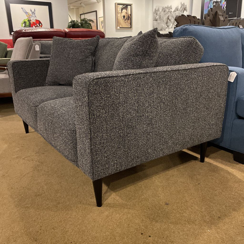 A contemporary charcoal grey two-seater loveseat with square arms and tapered black legs, shown in a furniture showroom.