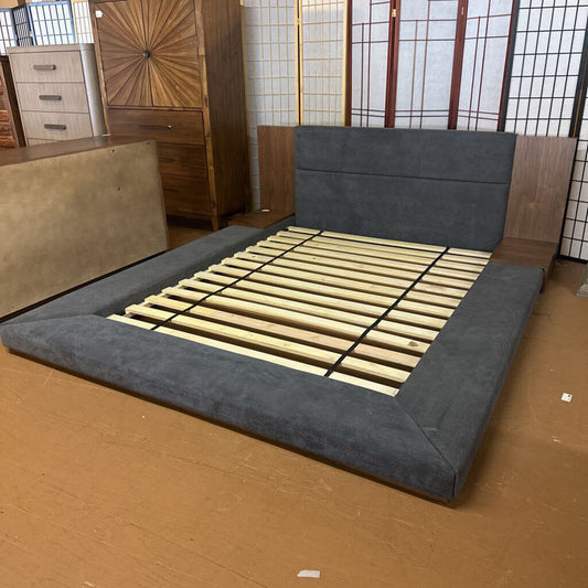 Gray upholstered bed frame with wooden slats on a wooden floor.