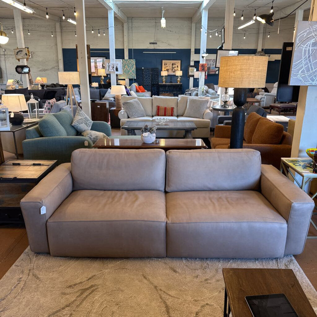 Beige sofa in a furniture store with various other furniture pieces in the background.