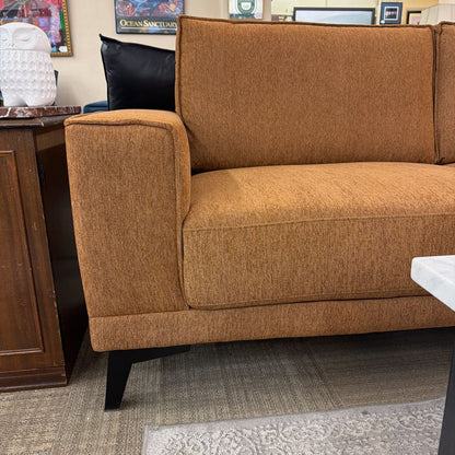 Brown sofa in a room with a desk and framed pictures on the wall.