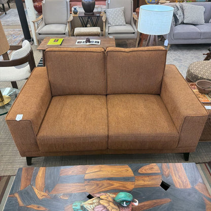 Brown sofa in a furniture store setting with other furniture items in the background.