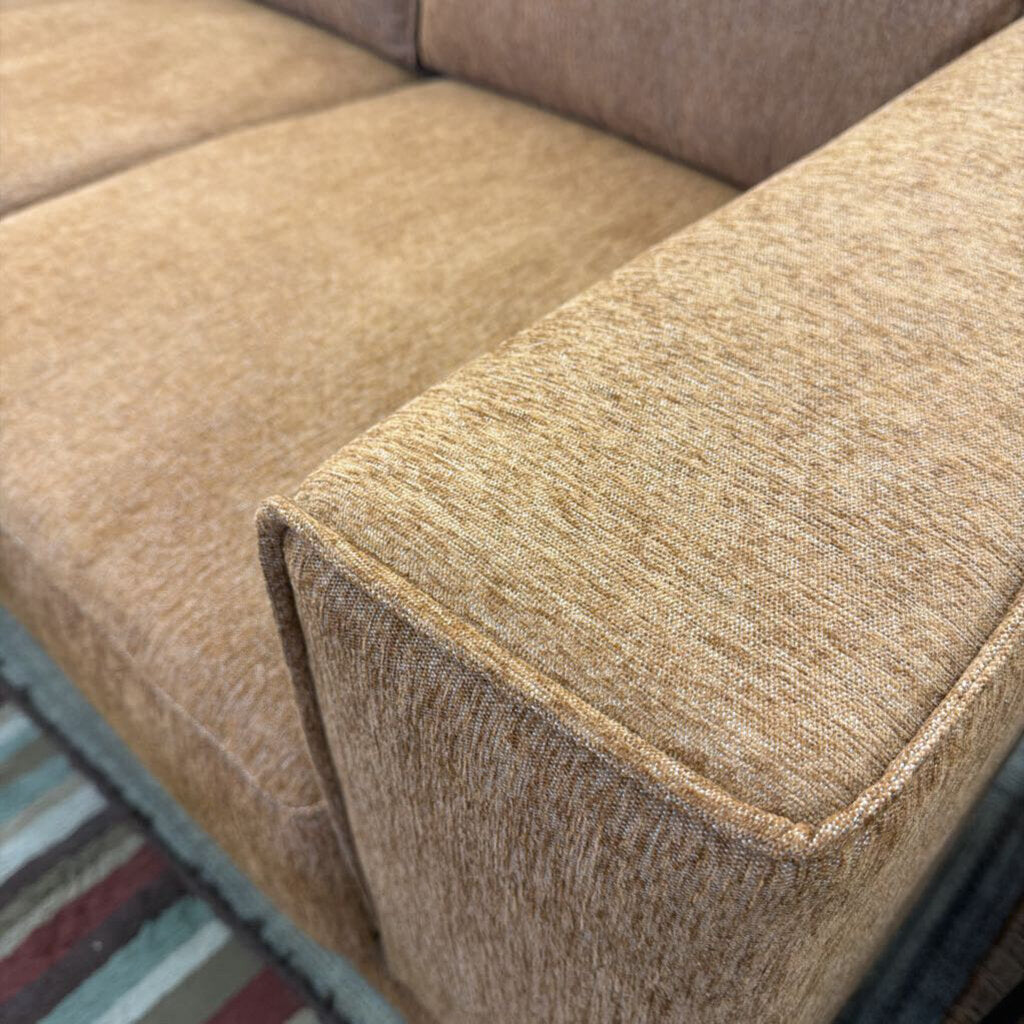Close-up of a brown textured sofa corner with a multicolored rug in the background.