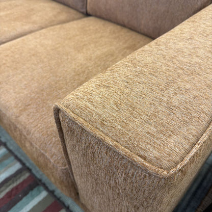 Close-up of a textured brown sofa corner with a multicolored rug in the background.