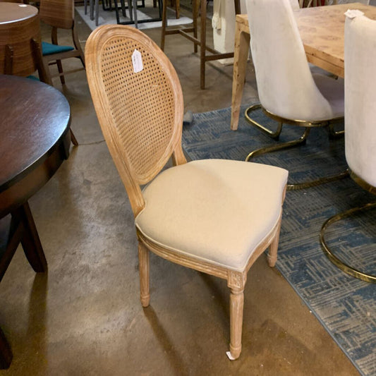 Chair with wicker back and beige cushion on a concrete floor with other furniture in the background