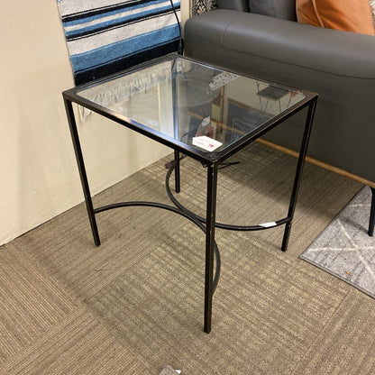 Glass side table with black metal frame in a room setting.