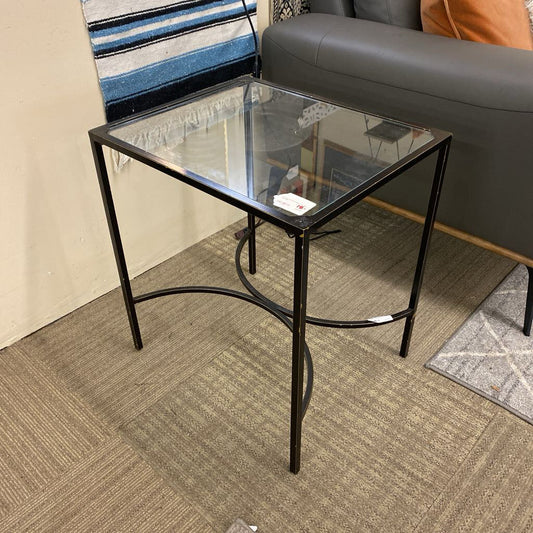 Glass side table with black metal frame in a room setting.