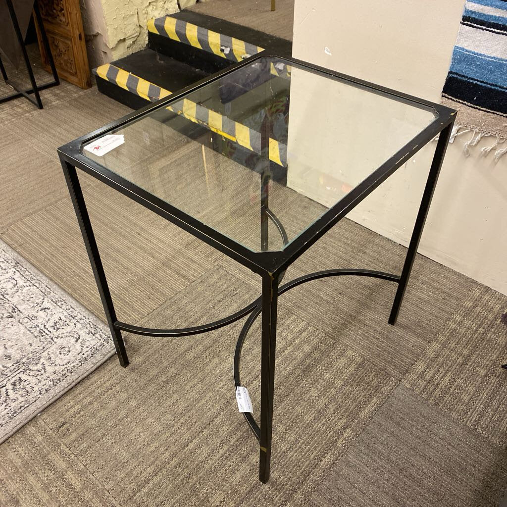 Glass side table with black metal frame on a carpeted floor