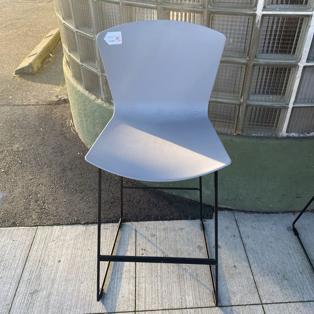 Gray bar stool with black metal legs on a concrete floor.