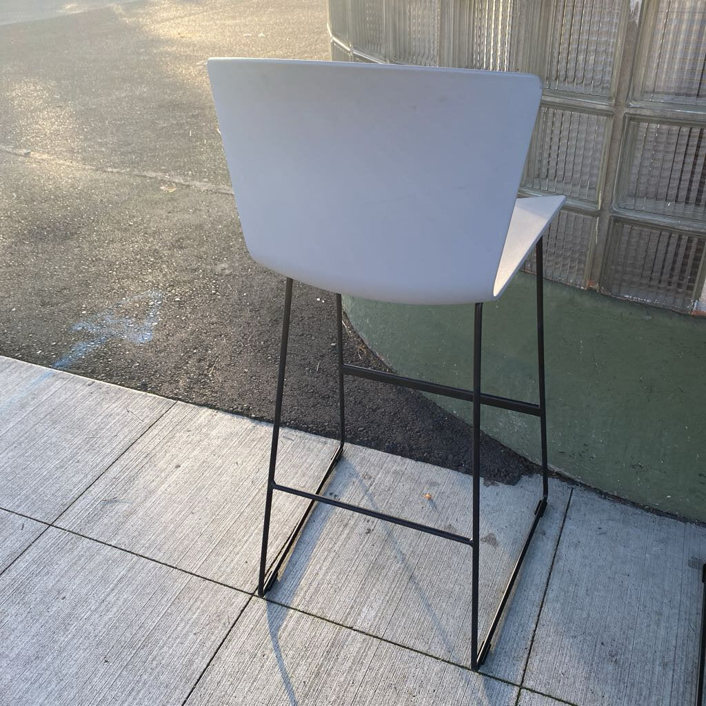 White bar stool with black metal legs on a tiled floor.