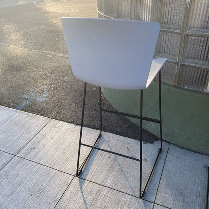 White bar stool with black metal legs on a tiled floor.